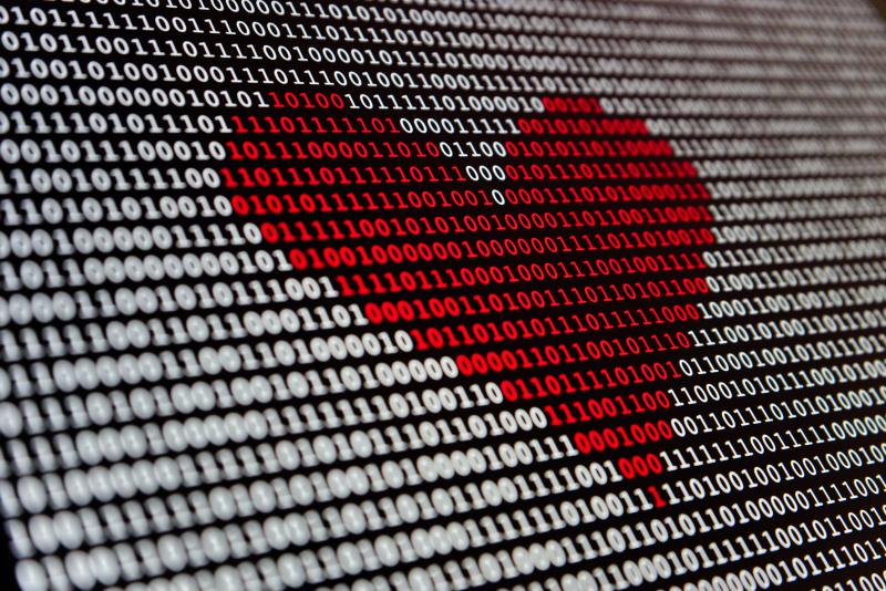 A screen full of ones and zeroes, some of which are colored red and form the shape of a heart.